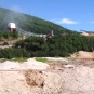 Photographie couleur d’une mine avec une roche blanche au premier plan, un bâtiment et des collines vertes à l’arrière-plan