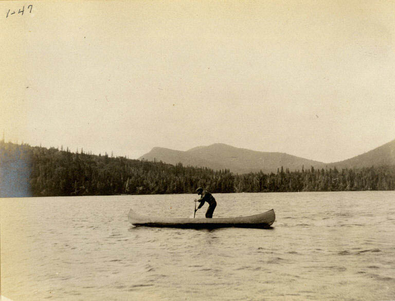 Photographie noir et blanc d’un homme en canot avec un paysage vallonné à l’arrière-plan