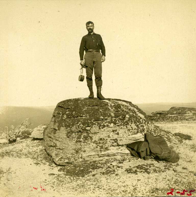 Photographie noir et blanc d’un homme debout sur un gros bloc