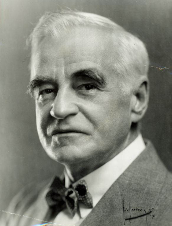 Photographie noir et blanc d’un homme aux cheveux gris en costume et nœud papillon