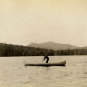 Photographie noir et blanc d’un homme en canot avec un paysage vallonné à l’arrière-plan