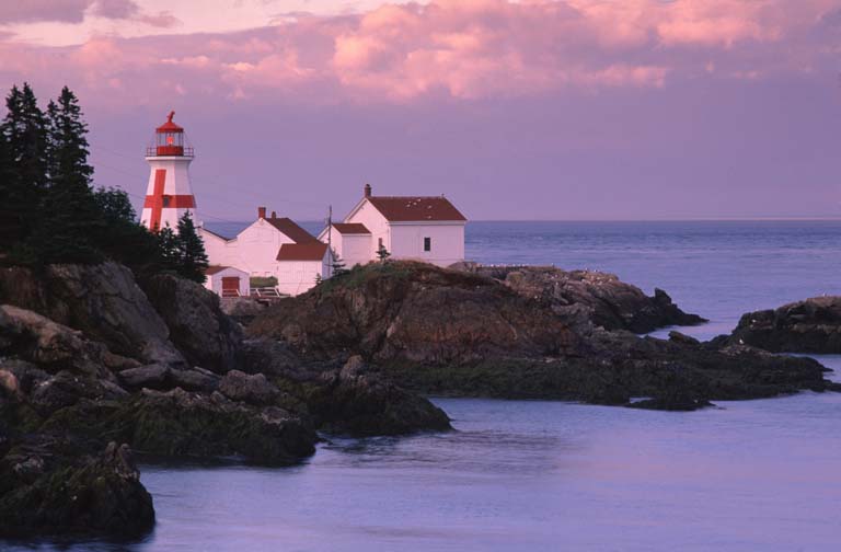 Photographie couleur d’un littoral rocheux, de l’océan et d’un phare rouge et blanc